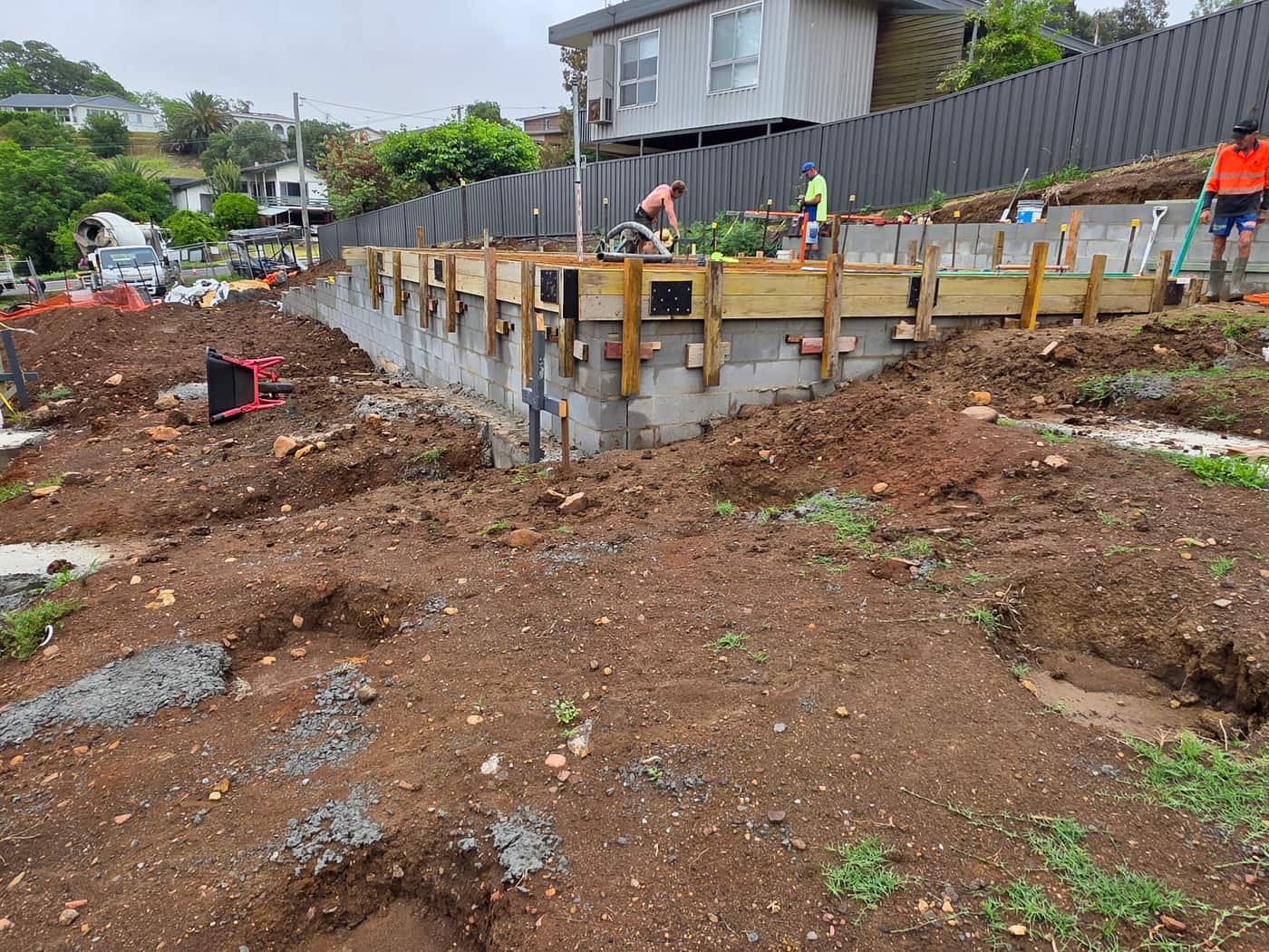 Timber edge forms braced along a block wall on a sloping site, with the crew working along the top