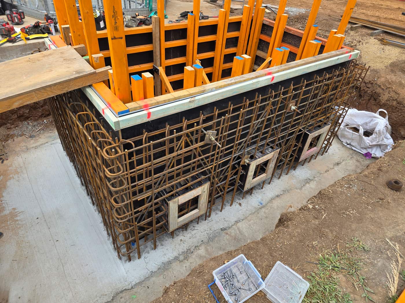 A reinforcement cage tied around a concrete pit, with the wall forms standing inside it and box outs left for the pipes